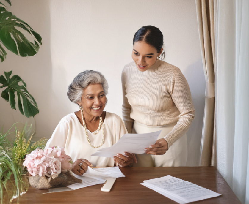 A younger woman helping an older woman review pre-planning paperwork at home
